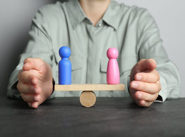 Gender equality concept. Woman with male and female figures on scales at dark table, closeup
